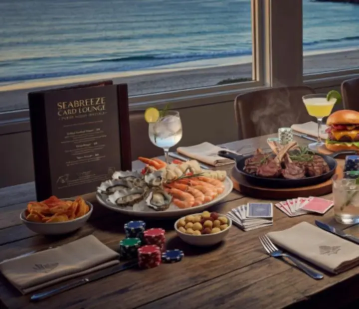 Share plates, seafood and cocktails arranged beside a green felt poker table in a coastal restaurant.